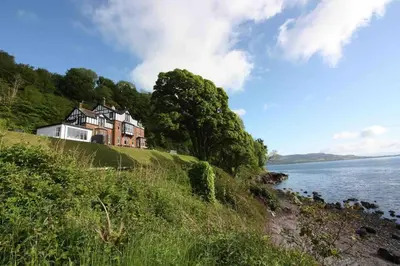 a house on a hill next to a body of water at The Apartment - Chandlers in Ascog