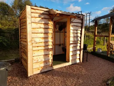 a wooden outhouse with a door in a yard at Sunset View Shepherds Hut in Dalmally