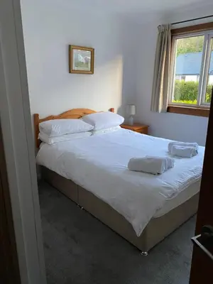a bedroom with a bed with white sheets and a window at Lyn leven cottages in Ballachulish