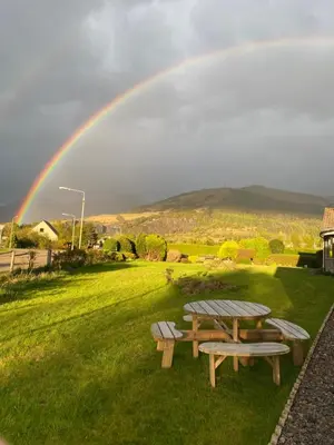 a rainbow in the sky with a picnic table and benches at Lyn leven cottages in Ballachulish