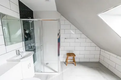 a white bathroom with a shower and a stool at Westertonhill Lodges - Private Hot Tub Hire Available in Balloch