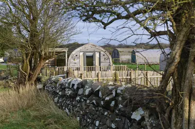 a log cabin with a fence and a stone wall at The Galloway Steading- The Bee Hive Couples Retreat with Hot Tub and Fire Pit in Glenluce