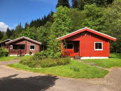 a couple of cabins in a forest with trees at Pucks Glen Lodges - Cosy Lodges in a Woodland Setting in Dunoon