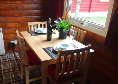 a wooden table with a bottle of wine and a plant at Pucks Glen Lodges - Cosy Lodges in a Woodland Setting in Dunoon