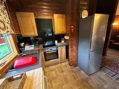 a kitchen with a stainless steel refrigerator and wooden cabinets at Pucks Glen Lodges - Cosy Lodges in a Woodland Setting in Dunoon