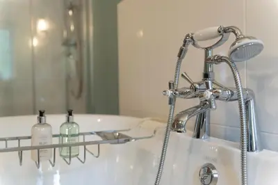 a bathroom with a bath tub with a shower and a sink at Steading Cottage - 50m from the beach in Port Appin