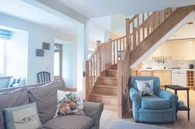 a living room with a couch and a stair case at Steading Cottage - 50m from the beach in Port Appin