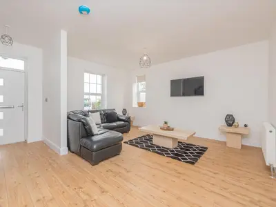 a living room with a leather couch and a tv at The Wee White Cottage in Bannockburn