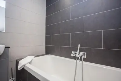 a white bath tub in a bathroom with gray tiles at Stylish Loch Lomond lodge in stunning surroundings in Balloch