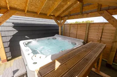 a hot tub on a deck with a wooden roof at Fulshaw Mill Holidays in Stewarton