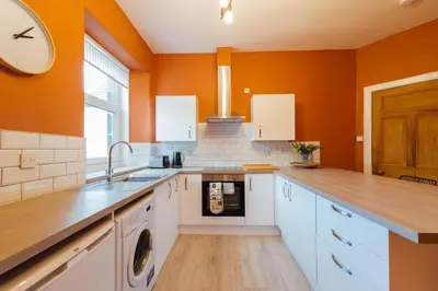 a large kitchen with orange walls and white cabinets at The Riverside Apartment (free parking) in Stirling