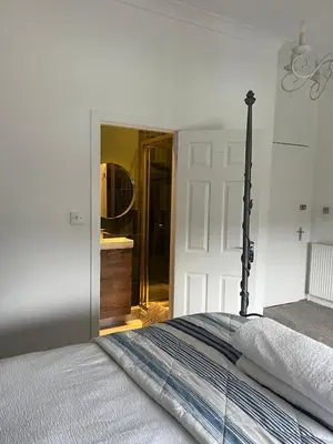 a white bedroom with a bed and a bathroom at Giffnock Rooms in Giffnock