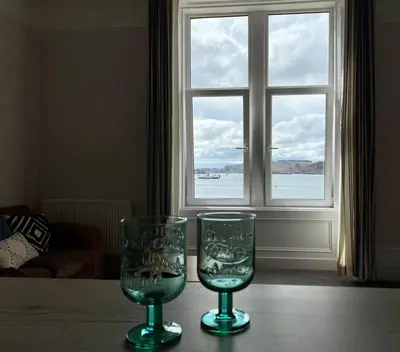 two glasses sitting on a table in front of a window at Westbay Seafront Apartment in Oban