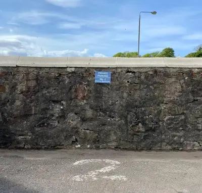 a stone wall with a blue sign on it at Westbay Seafront Apartment in Oban