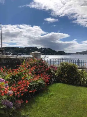 a garden with flowers in front of a body of water at Westbay Seafront Apartment in Oban