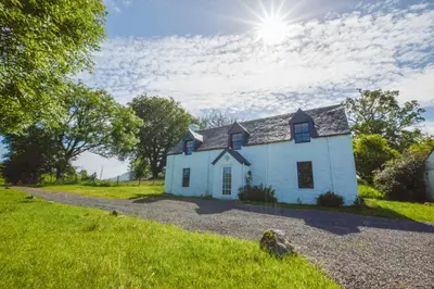 a white house on a hill with the sun behind it at Achanlochan Farm in Taynuilt