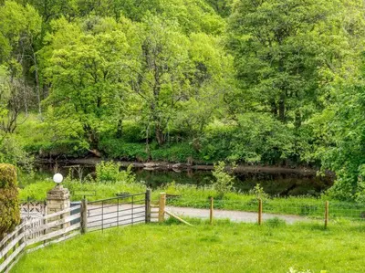 a fence in the grass next to a body of water at 3 Bedroom luxury home, hot tub, stunning views of Killin, sitting on the River Dochart in Killin