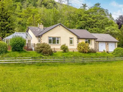 a house in the middle of a field with a fence at 3 Bedroom luxury home, hot tub, stunning views of Killin, sitting on the River Dochart in Killin
