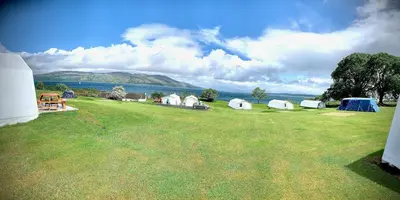 a large grass field with tents and a body of water at Glamping at Shieling Holidays Mull in Craignure