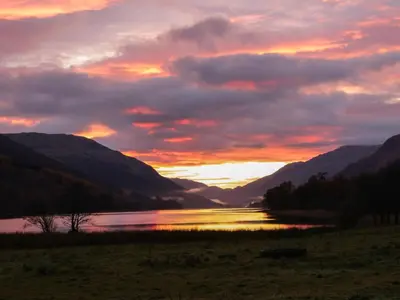 a sunset over a body of water with mountains at Inglis Nook Cottage in Lochearnhead