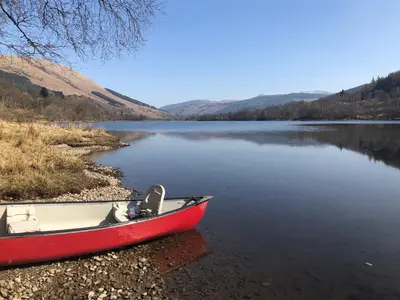 a red boat sitting on the shore of a lake at Inglis Nook Cottage in Lochearnhead