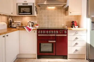 a kitchen with a red oven and white cabinets at The Old Farmhouse in Balloch
