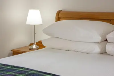 a bed with white pillows and a lamp on a table at Branter Lodge in Strachur