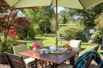 a wooden table under an umbrella in a yard at Strone House in Helensburgh