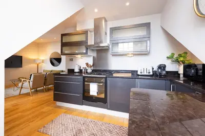 a kitchen with black appliances and a living room at JOIVY Luxury Flat near Edinburgh Castle in Edinburgh