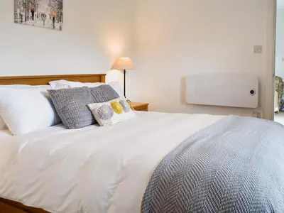 a white bed with pillows and a tv on the wall at Boatman's Cottage At Invernian Mor in Inverinan Beg