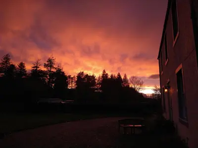 a sunset with a red sky with a building and a bench at Kirkland House B&B in Tarbert