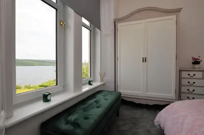 a bedroom with two windows and a green bench next to a bed at Findhorn Upper Apartment in Kames