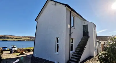 a white house with stairs next to a body of water at Findhorn Upper Apartment in Kames