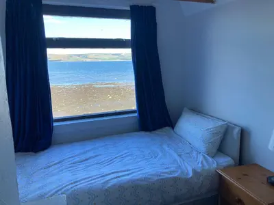 a bedroom with a window with a bed and a beach at Waters Edge in Stranraer