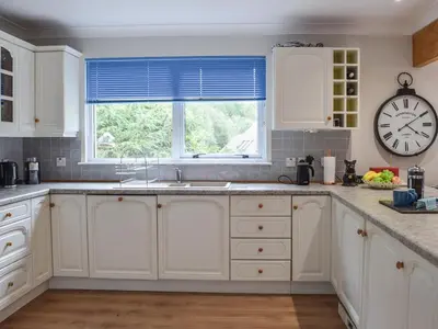 a kitchen with white cabinets and a clock on the wall at Tamarchan Lodge in Ballachulish