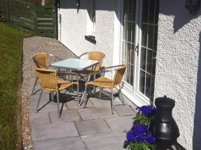 a patio with a table and chairs next to a window at Glenfruin Lodge in Helensburgh