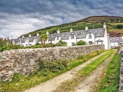 a row of houses on a hill with a stone wall at The Apostles in Catacol