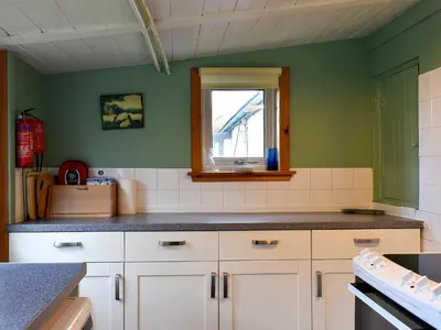 a kitchen with white cabinets and a window at Burnside Cottage in Sliddery