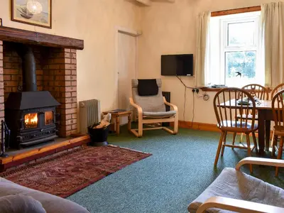 a living room with a fireplace and a chair at Burnside Cottage in Sliddery