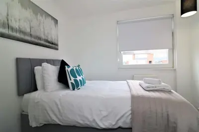 a white bedroom with a large bed with a window at Signature - Barons Court in Paisley