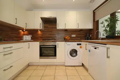 a kitchen with white cabinets and a washer and dryer at Signature - Barons Court in Paisley