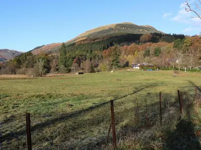a fence in a field with a mountain in the background at Puidrac Cottage in Lochearnhead