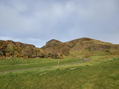 a road in a field with a mountain in the background at Lovely 2 bedroom flat in the heart of the city in Edinburgh