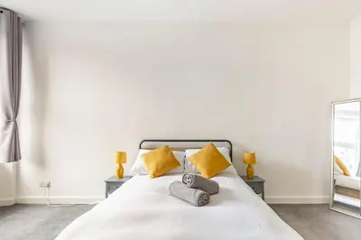a bedroom with a white bed with yellow pillows at Spacious stylish centraly located flat near beach in Largs
