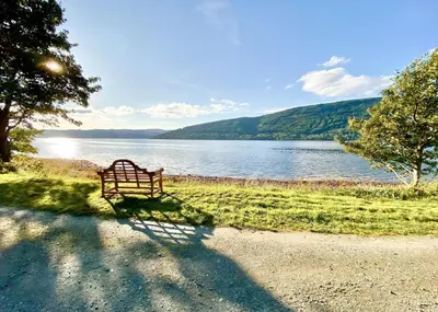 a bench sitting on the grass next to a lake at Seal Point Cabin - Luxury Glamping in Cairndow