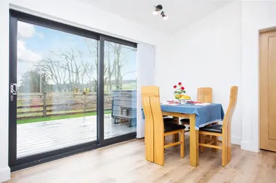 a dining room with a table and chairs and a large window at Shiphorns luxury cabin with a hot tub in Eddleston