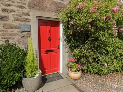 a red door on a stone building with plants at Greystones Cottage in Crieff