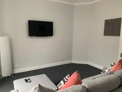 a living room with a couch and a tv on a wall at Nelson st (ANNAN) in Largs