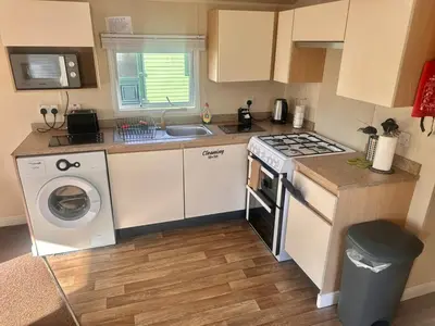 a small kitchen with a stove and a washing machine at Two Bedroom Willerby Caravan Located in Uddingston, Glasgow at Maryville Caravan Site in Uddingston
