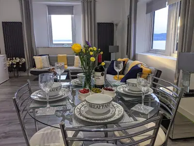a dining room table with dishes and flowers on it at Strathclyde Cottage North in Skelmorlie